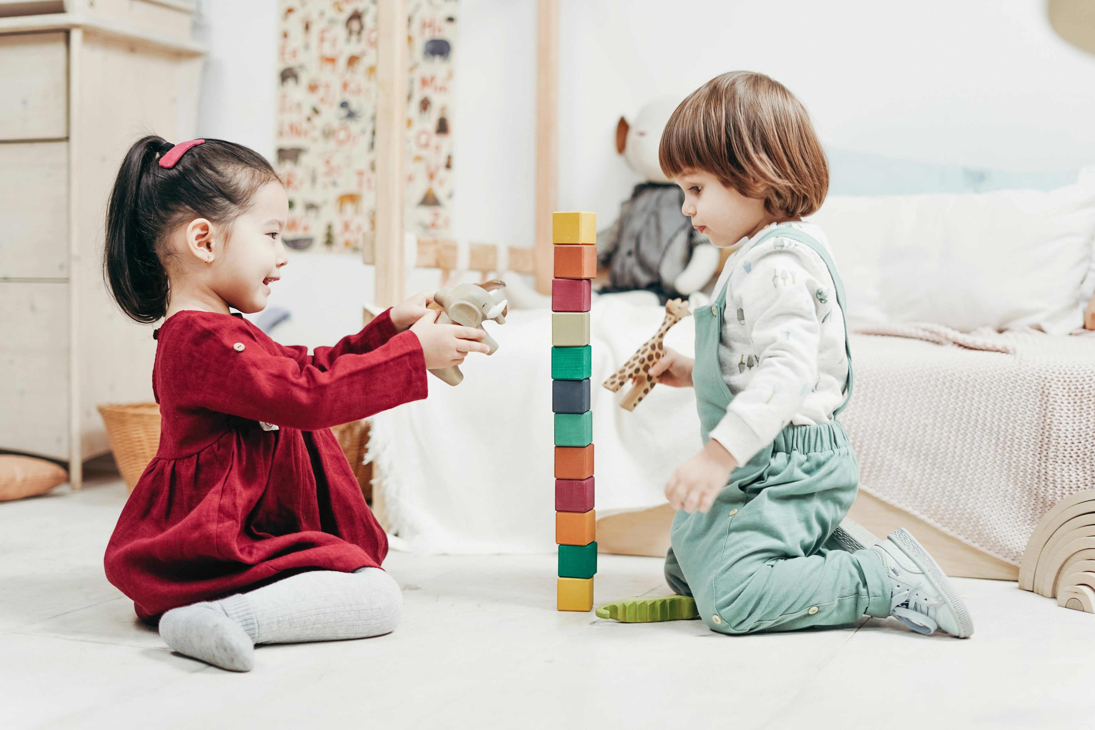 Two children playing with colorful blocks on a light-colored floor.